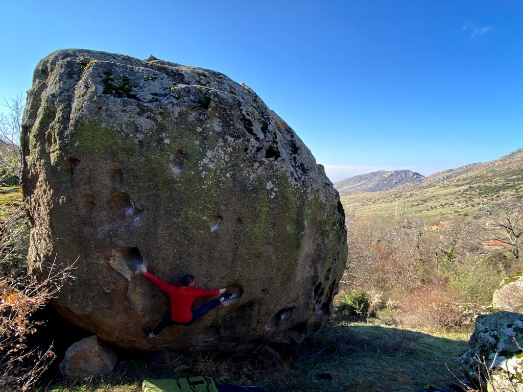 Climber spread wide on a problem at Dabnica between two small huecos with a heel hook matching one hand.