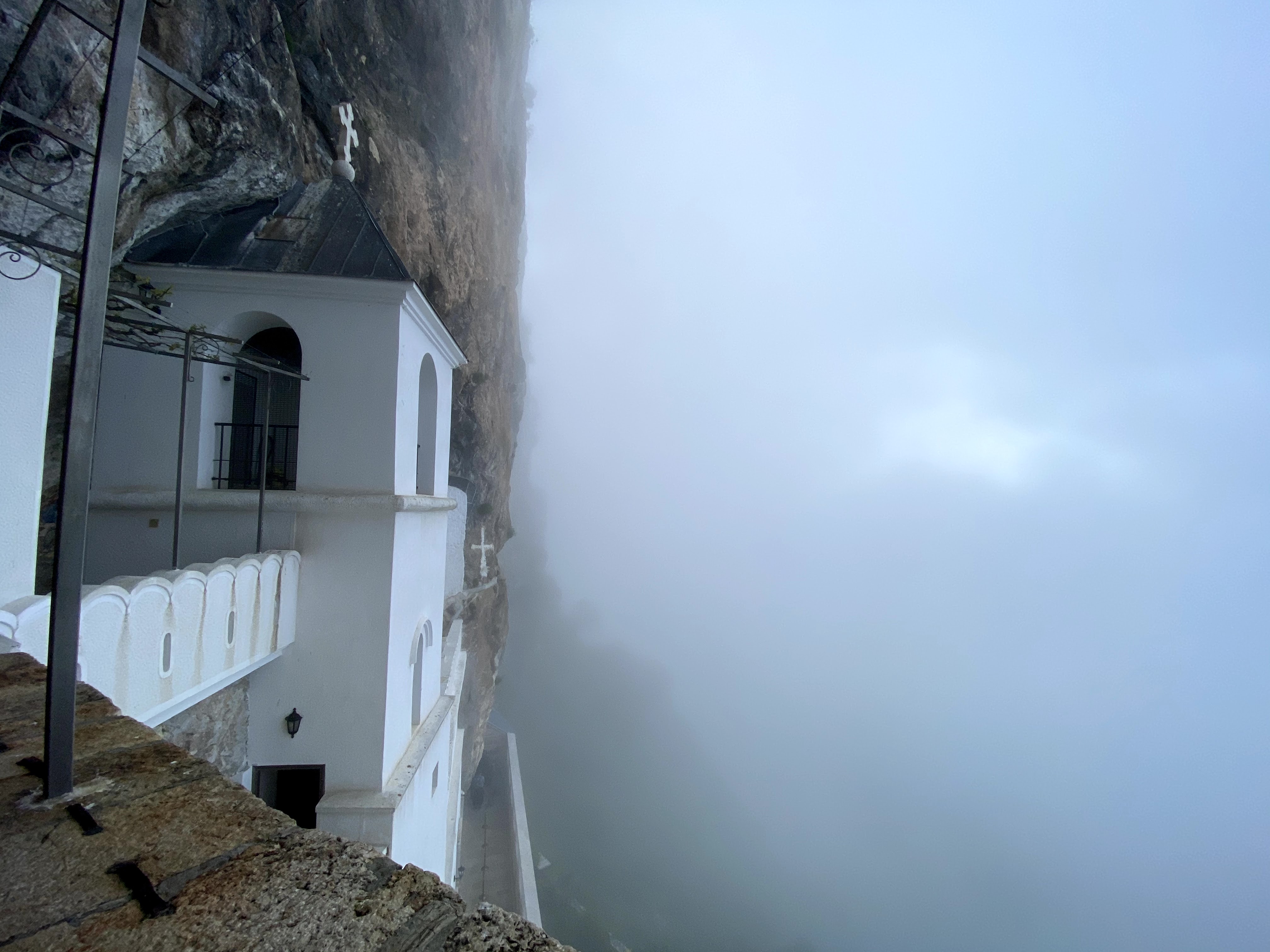 White Church of Ostrog Monastery set into a steep cliff face. Dramatically there is fog covering the view.