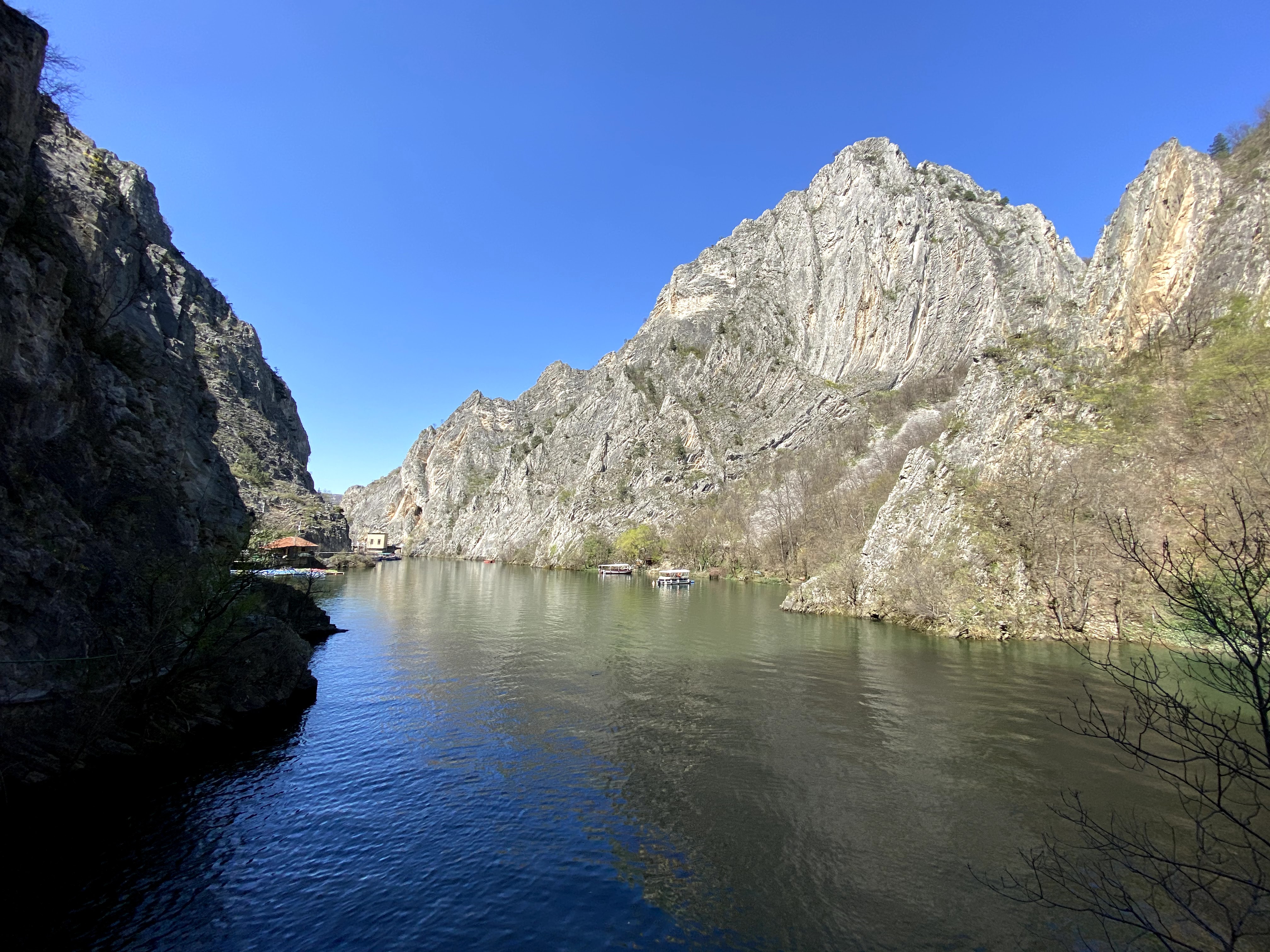Large open Matka Canyon with a river filled the bottom. There are a few tourist boats on the lake.
