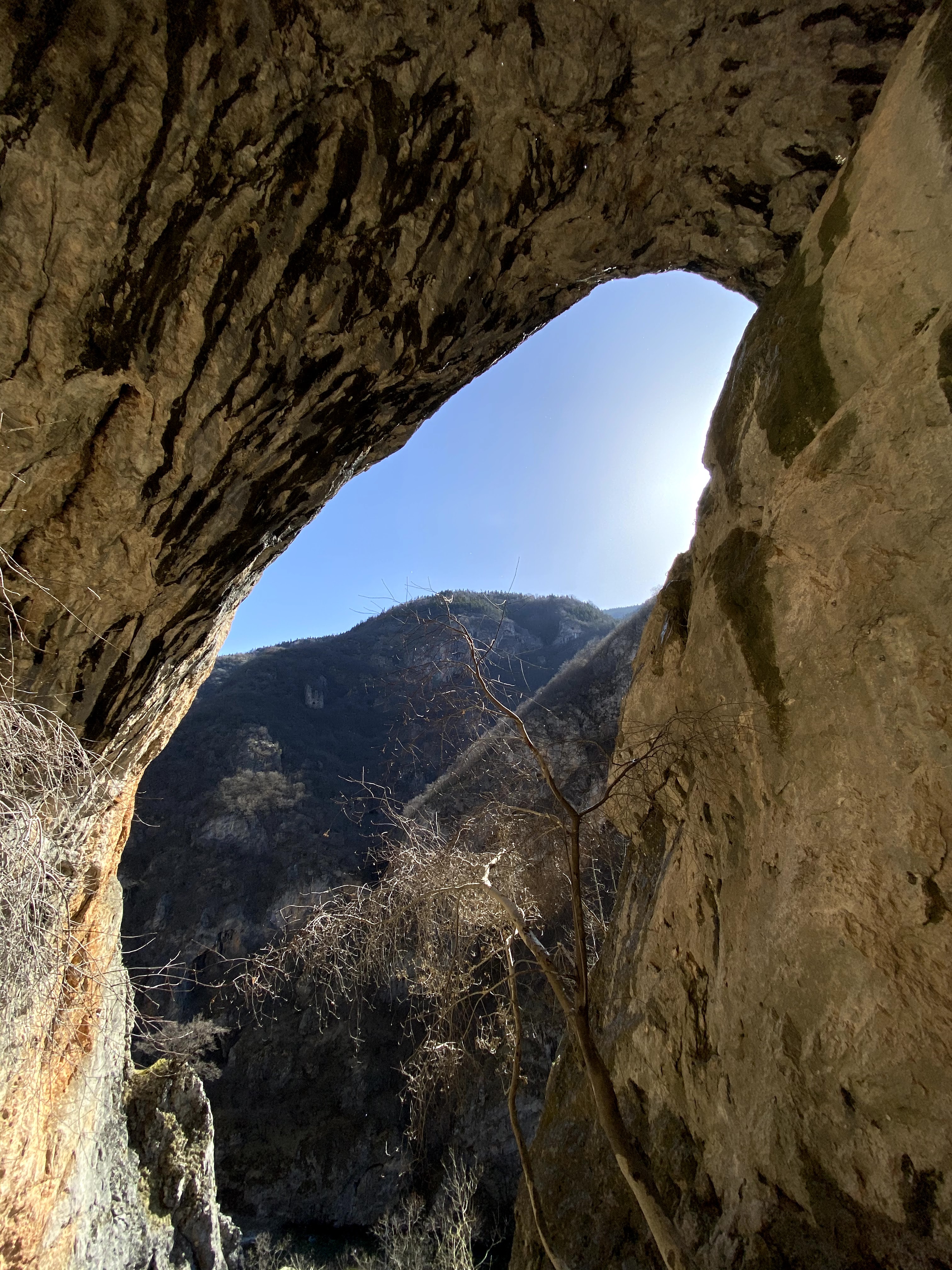 Looking out of the cave at Mavrovo with the lip of the cave framing the view out onto a steep mountain covered in trees.