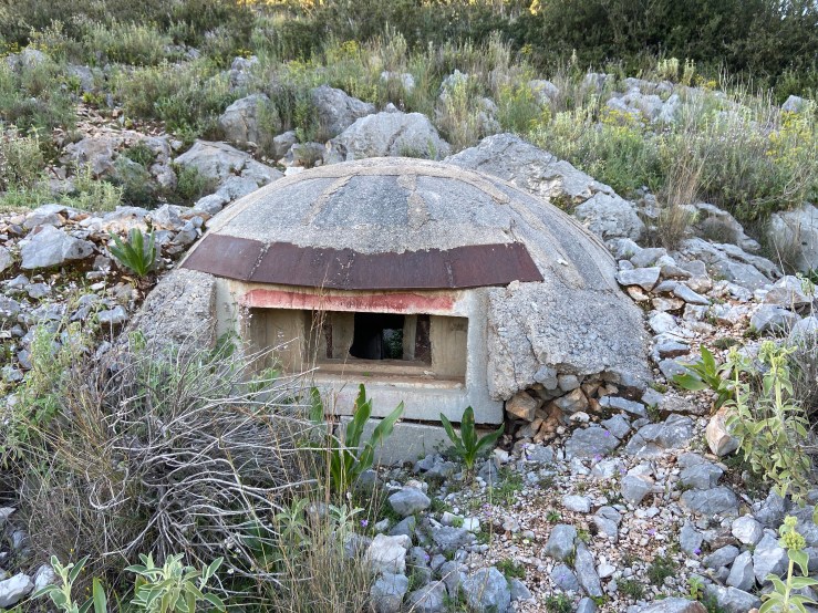 Mushroom shaped concrete bunker set into the rocky ground. There is a small lookout window. 