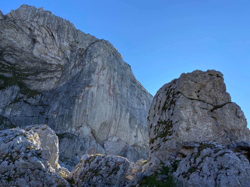 A huge mountain cliff overshadows the boulder field below. 