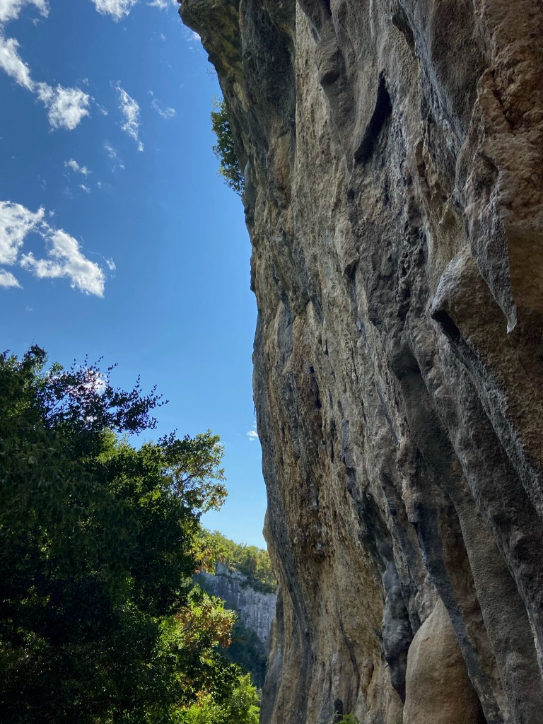 Large cliff dripping in grey and white tufas. The sky is blue in the background.