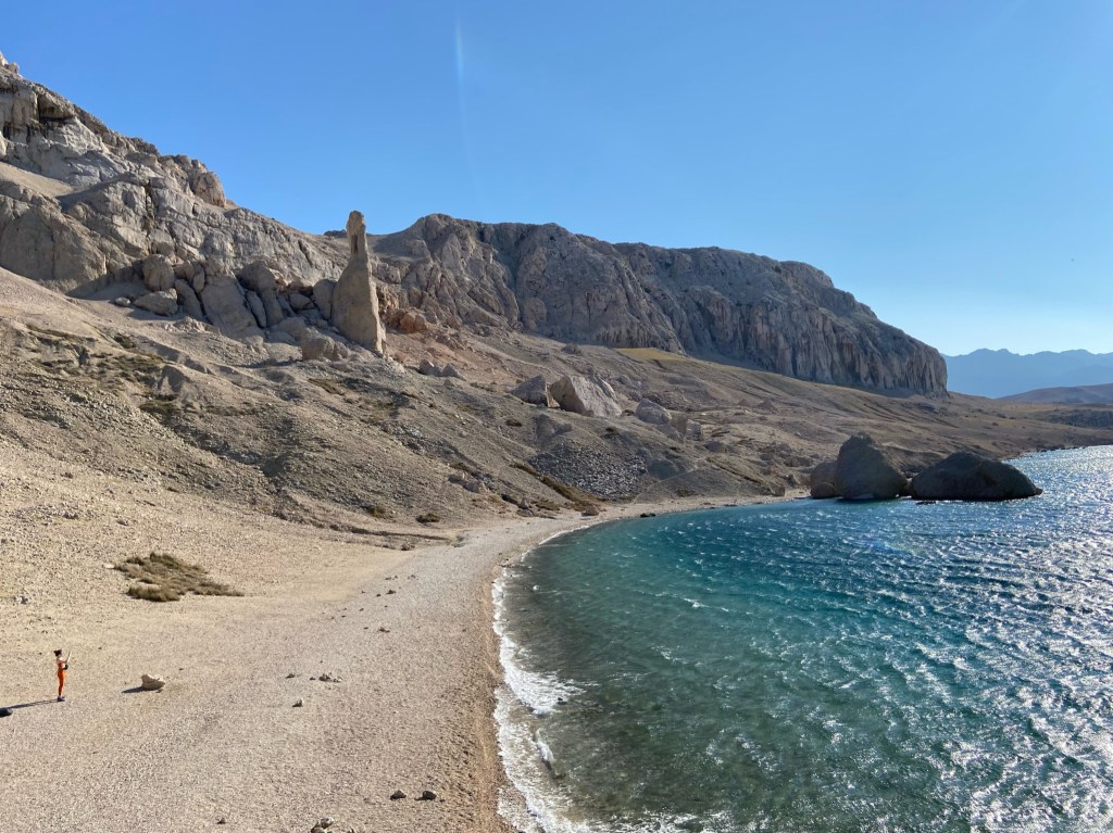 Moonscape landscape on the island of Pag. There is a bay with blue sea lapping onto the pebble beach.