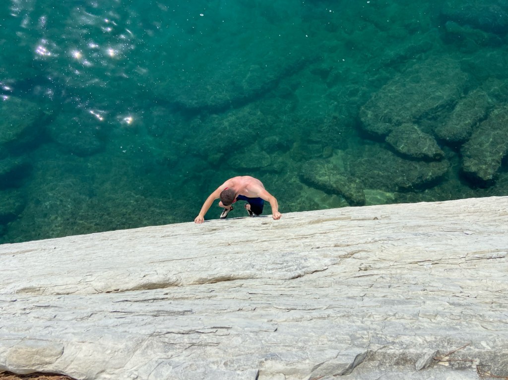 Man climbing on white cliff with the deep blue sea beneath them.