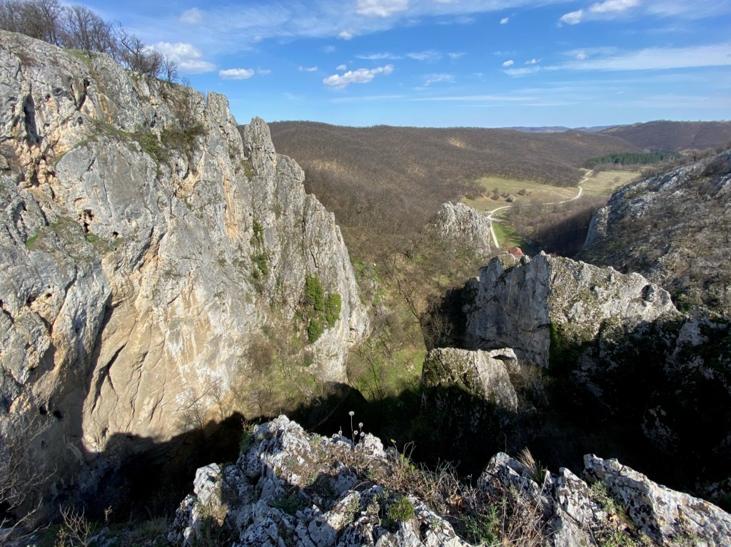 Craggy outcrops on a blue sky day with limestone rocks jutting out of the rolling hillside which is covered in leaf-less trees. 