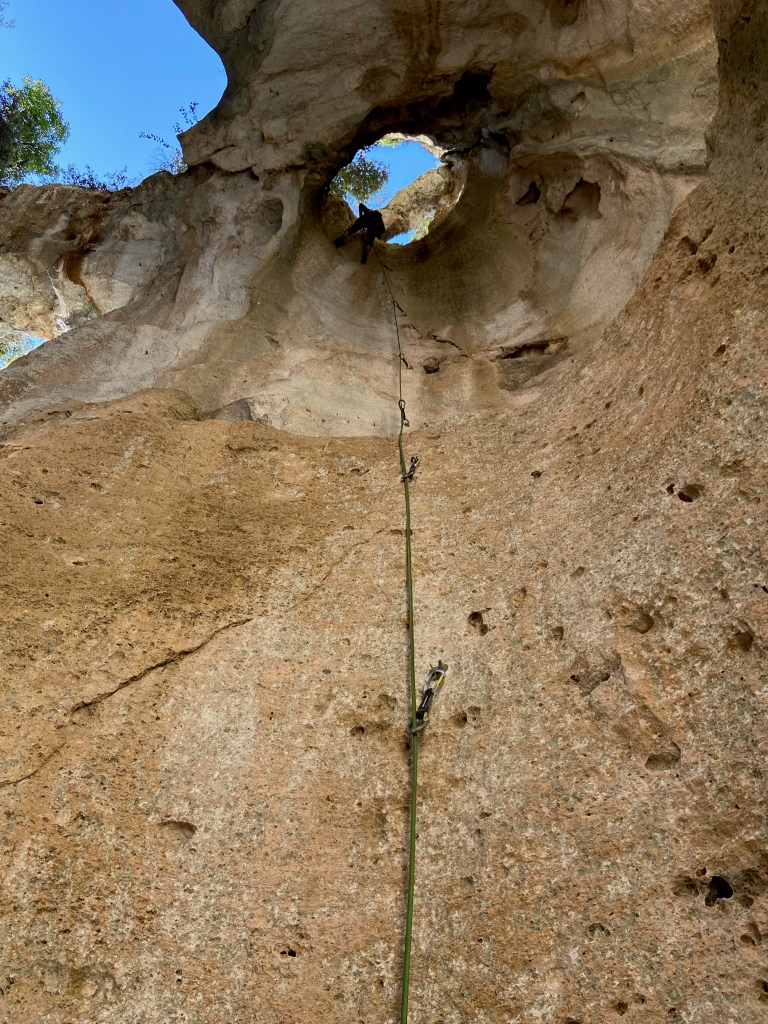 Climber at the top of a cylindrical pipe of limestone. There is a hole at the top with trees and the sky.