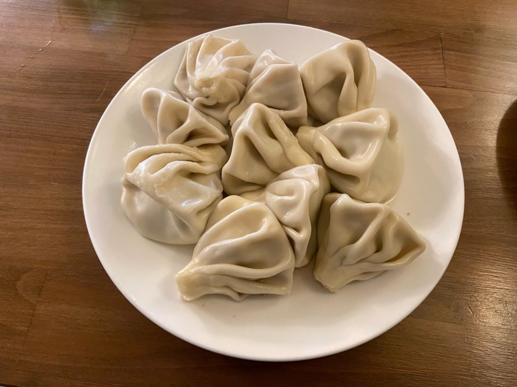 Plate with large filled white dumplings crimped together to form a handle for eating at the top. 