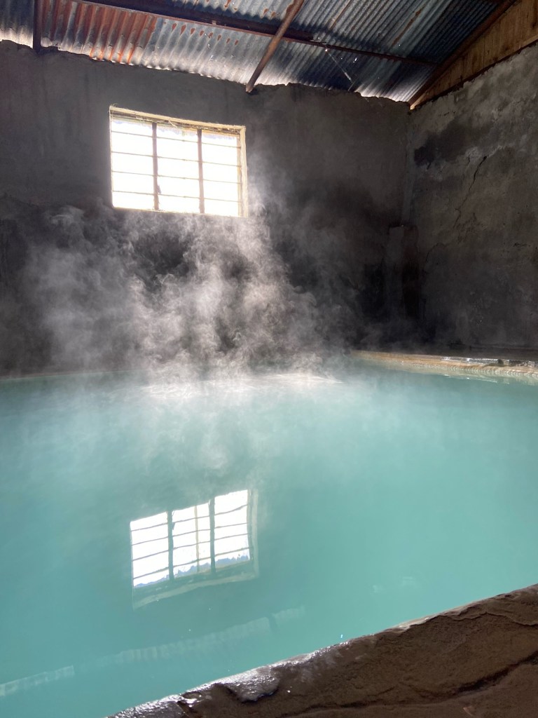A large hot steamy pool in concrete room with a tin roof and a small window.