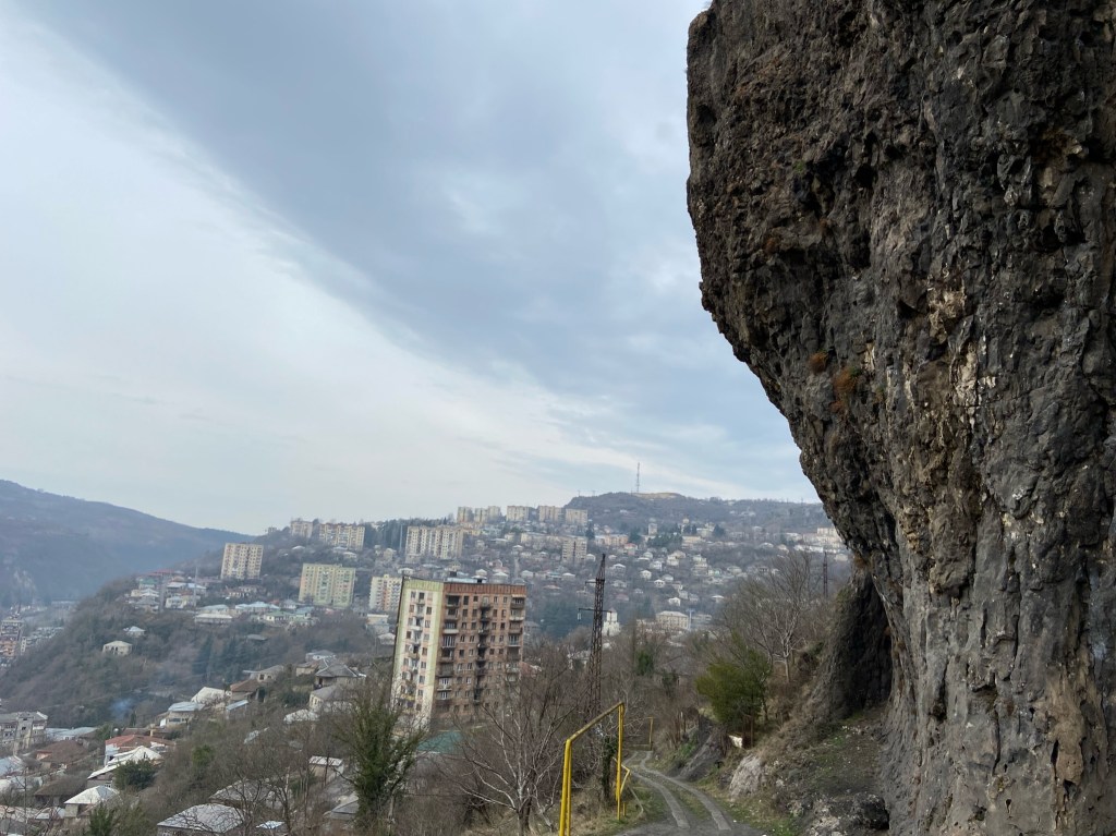 A steep and black limestone crag overlooking Chiatura. In the background there are old soviet tower blocks 