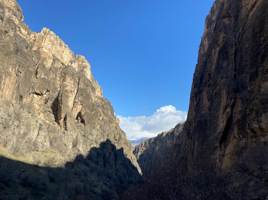 Steep and narrow limestone valley with one side of the valley casting a shower on the other. There is blue sky with clouds.