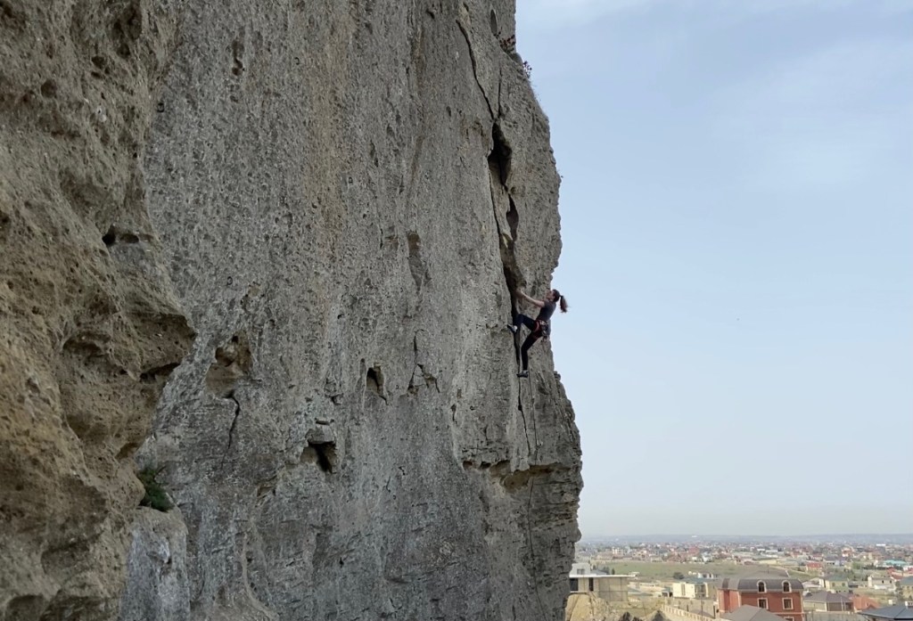 Climber lay backing up the undercut flake with houses in the background  