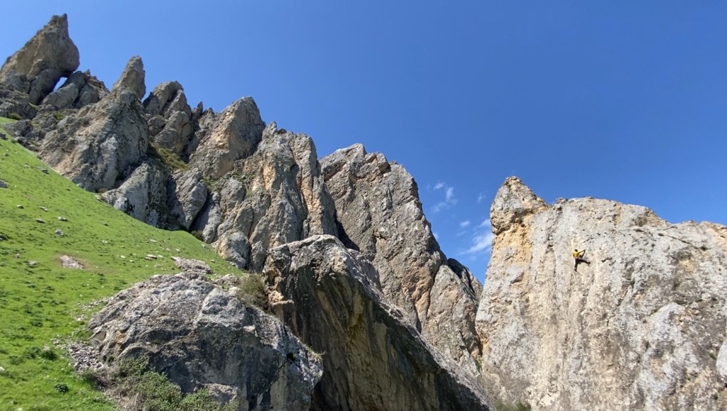 Climber on a large limestone pinnacle of rock which is a part of several pinnacles set within the steep grassy hillside. 