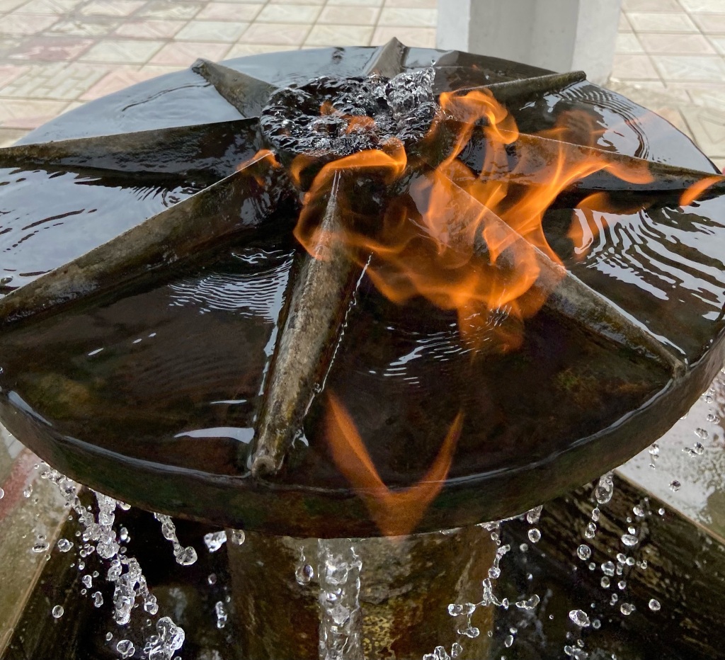 Orange flames appearing from a flowing metal water fountain. 