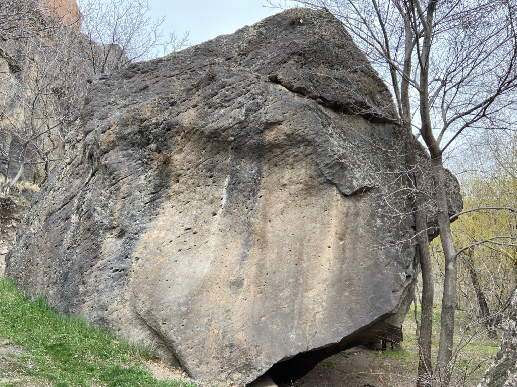 Large boulder with a smooth wall with pocketed rock around bare winter trees