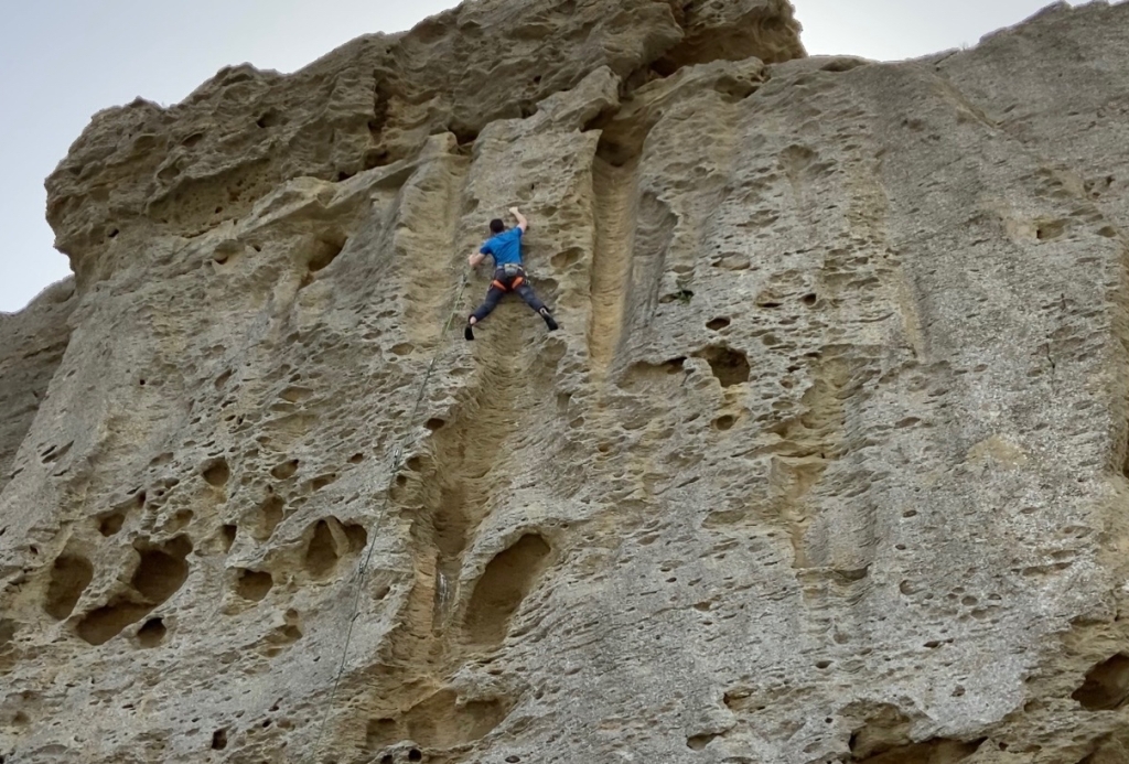 Climber on heavy featured and pocketed white limestone crag