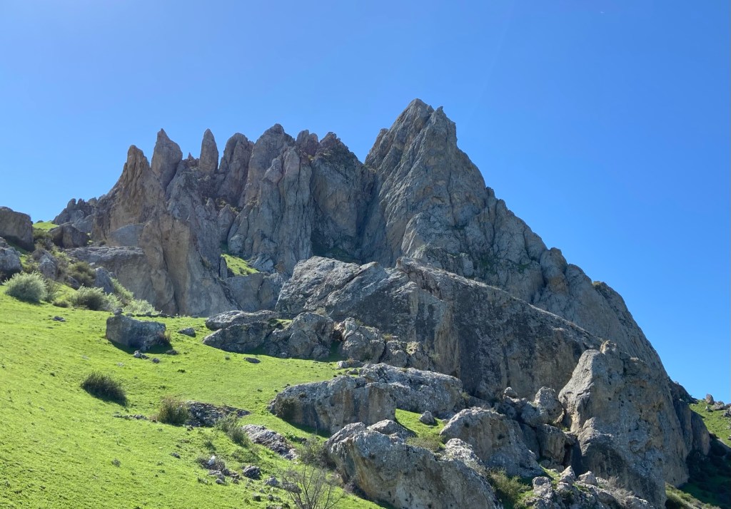 Large limestone pillars with lush green grass at the bottom and bright blue skies