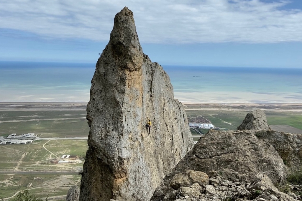 Climber on large limestone pinnacle with the blue Caspian Sea in the background