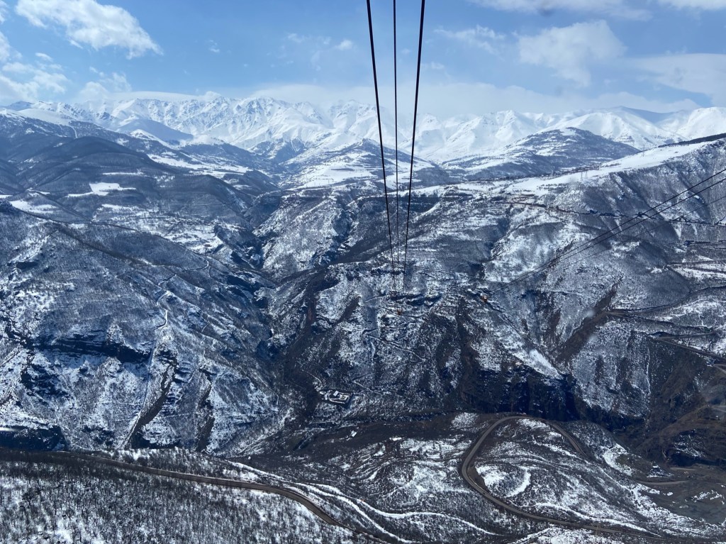 Cable car cables running down the valley. The landscape is covered in snow and there is a snaking road down at the valley floor.