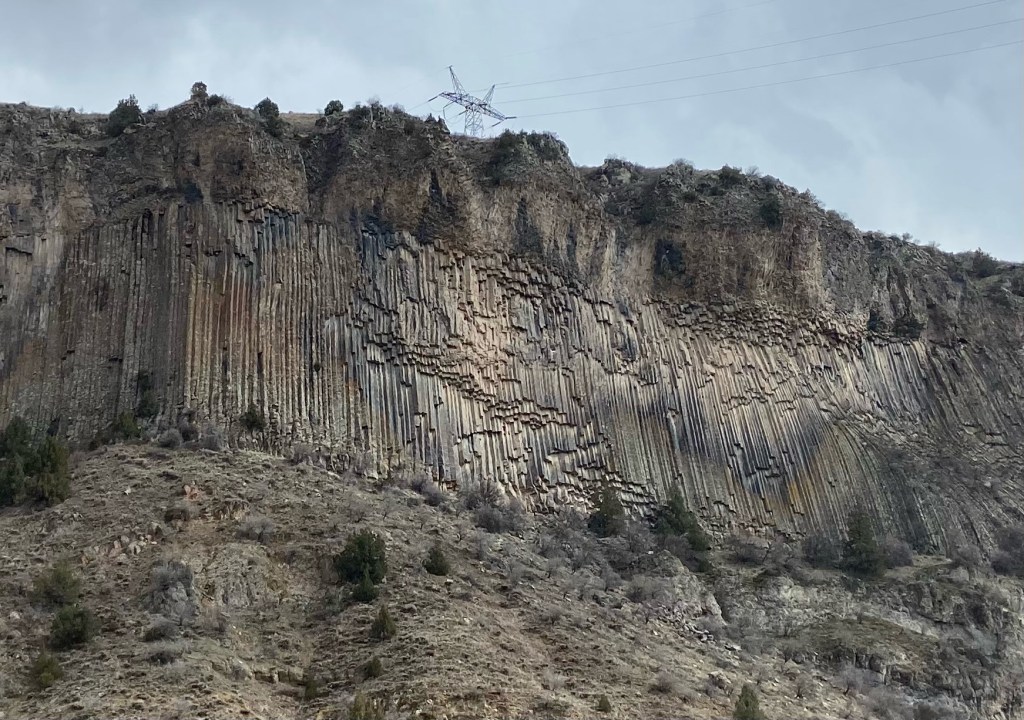Interesting basalt column formation, 3D long, geometric columns of different heights along a cliff with a large grassy bank leading up to it