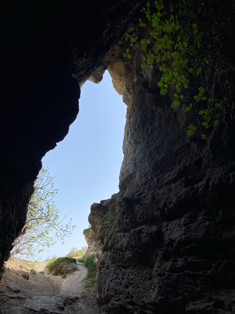 Looking out of the cave with the two steep sides silhouetting the blue sky outside  
