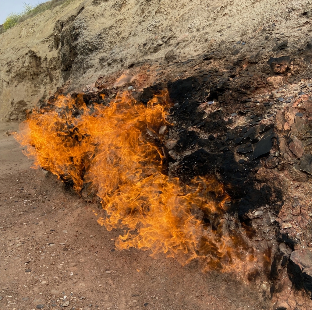 Big orange flames emerging from the rock. Around the flame are black carbon deposits on the rock 