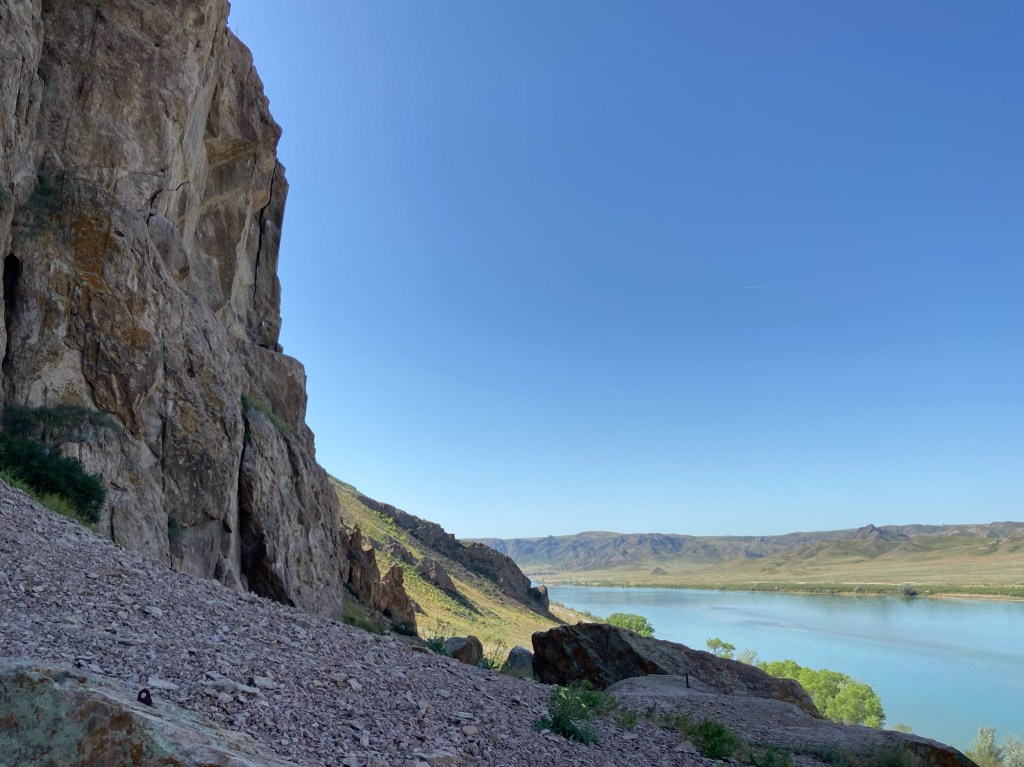 Rocky cliff with scree at the bottom. There is a river running through the bottom of the shallow gully