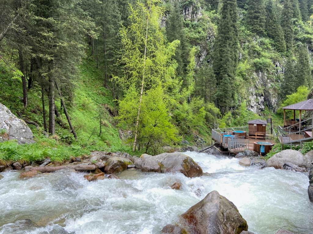 Fast river rapids with a wooden deck on one side with blue pools where the thermal water is piped into. 