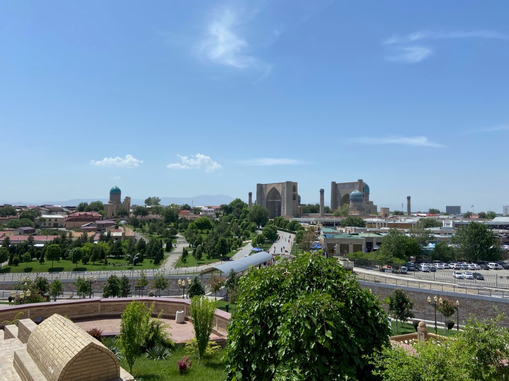 A view of the city where you can see the grand mausoleum complex towering above the more modern, smaller buildings. Throughout the landscape are blue tiled domes of religious sites
