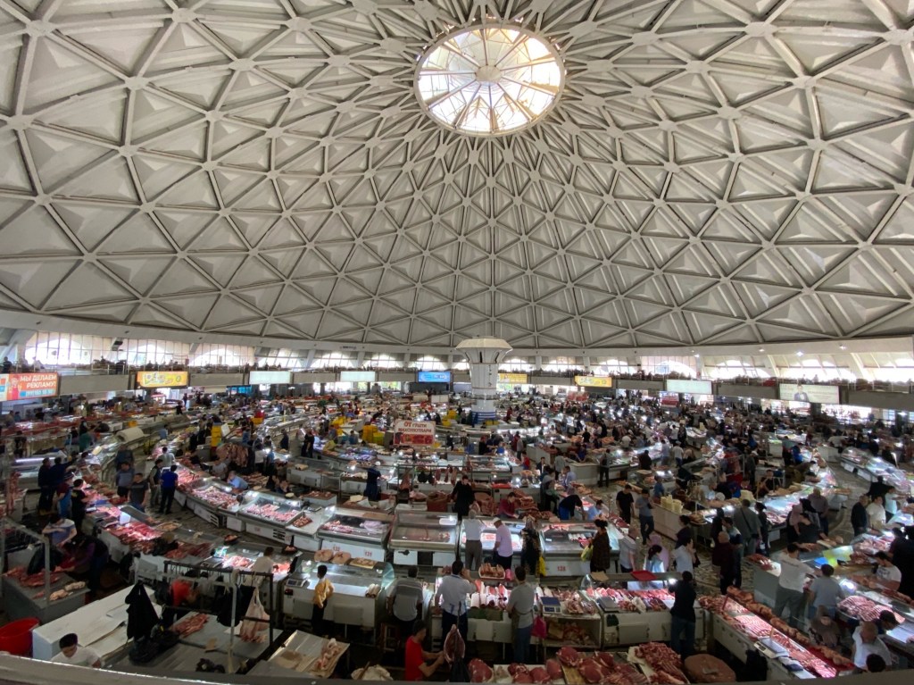 Large and busy market with lots of stalls expanding outwards in circles. There's a large domed ceiling above making the whole market look very grand   