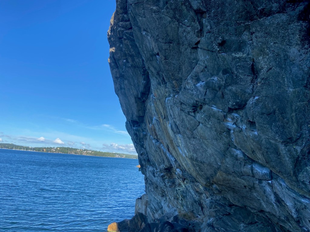 Steep granite rock overhanging onto the sea. In the background is the other side of the land.