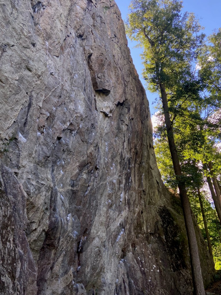 Slightly overhanging tall wall of granite rock. There are chalked holds up the face.
