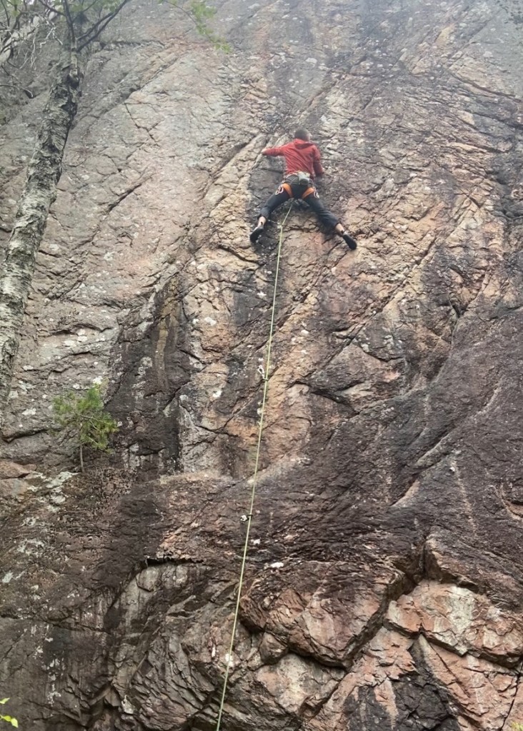 Climber on granite sport climb. The rock is a mixture of pink, grey and black in colour.