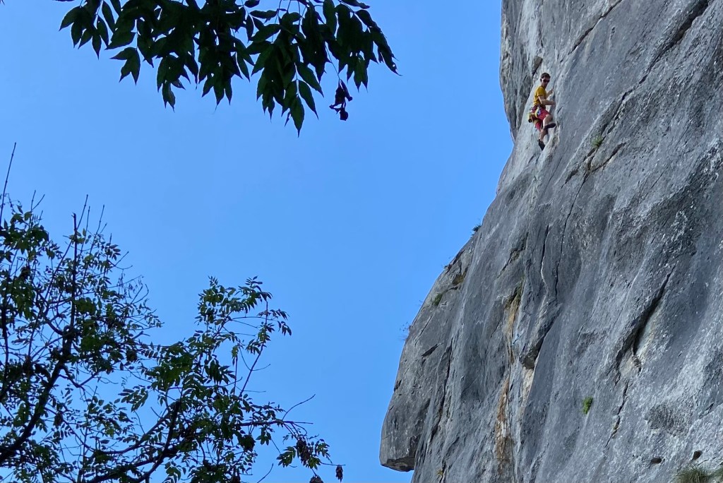 Climber on smooth grey limestone wall with blue skies 