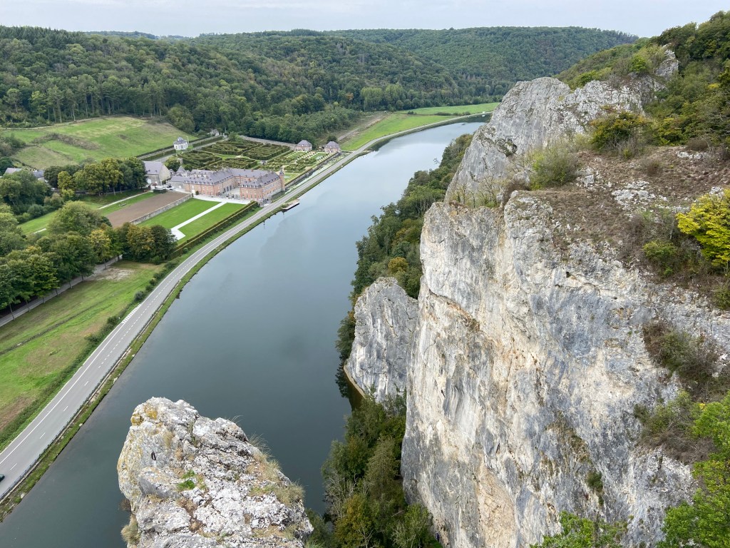 Limestone wall above a calm river. On the other side of the river is a chateau with maze like hedges and immaculate gardens