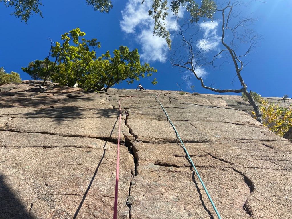 Climber in the sun on the granite cliff of Galgeberget. The sky is bright blue with a small amount of cloud.
