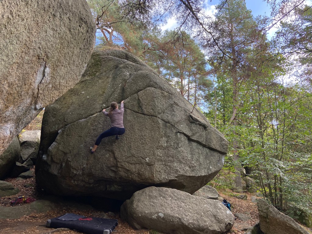 Climber bouldering and traversing upwards on the crack with a black bouldering pad beneath. 