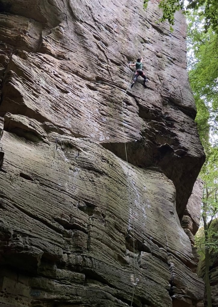 Climber on sandstone wall reaching to the next break in the rock where the hold is. 