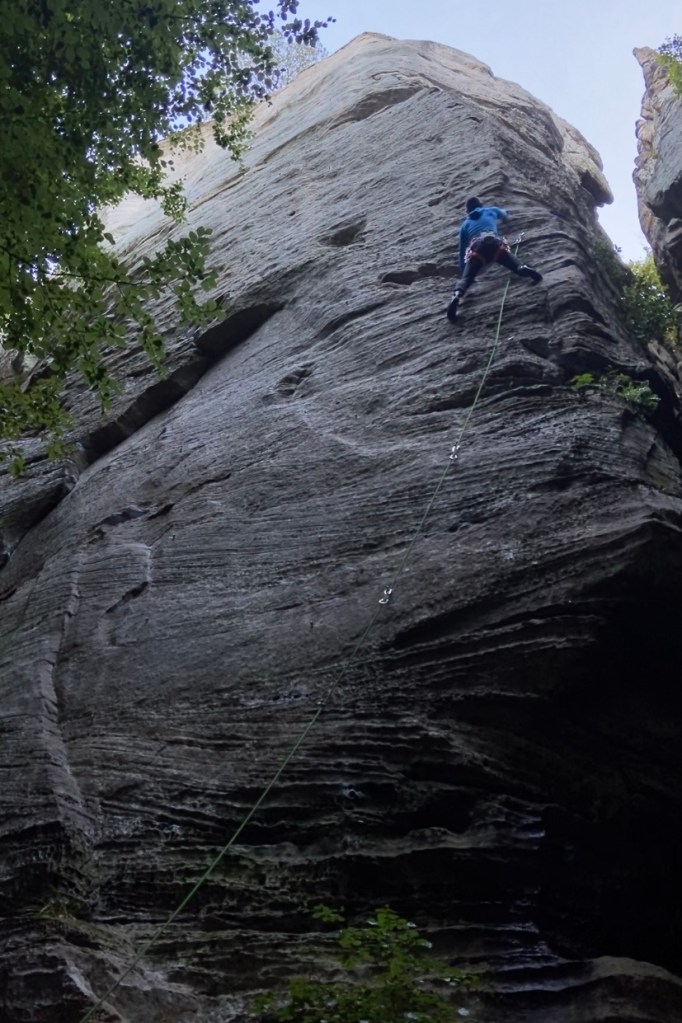Climber on sandstone wall with horizontal breaks in the rock.