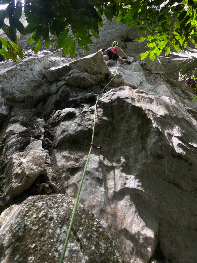Climber with green helmet under a steep section of rock at Bukit Takun