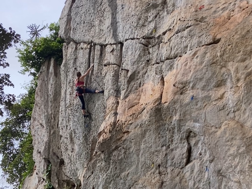 Climber on white pocketed limestone using water eroded runnels for hand holds and extending right leg outwards for balance.