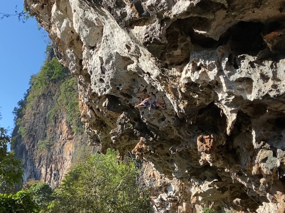 Climber making the clip on the steep limestone cave roof with featured pockets.
