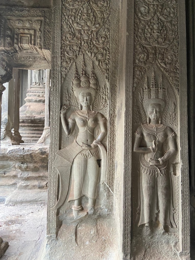 Ornate and large Devata carvings which are Hindu heavenly women with head dresses and elaborate necklaces and body jewellery. They're carved into a light coloured stone on the wall in Angkor Wat