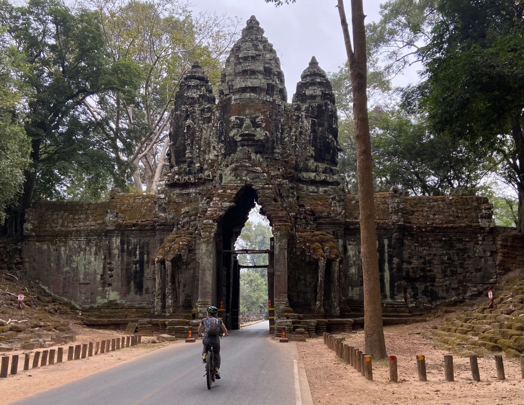 Cyclist cycling through an ancient archway in Angkor Wat complex with a backpack on