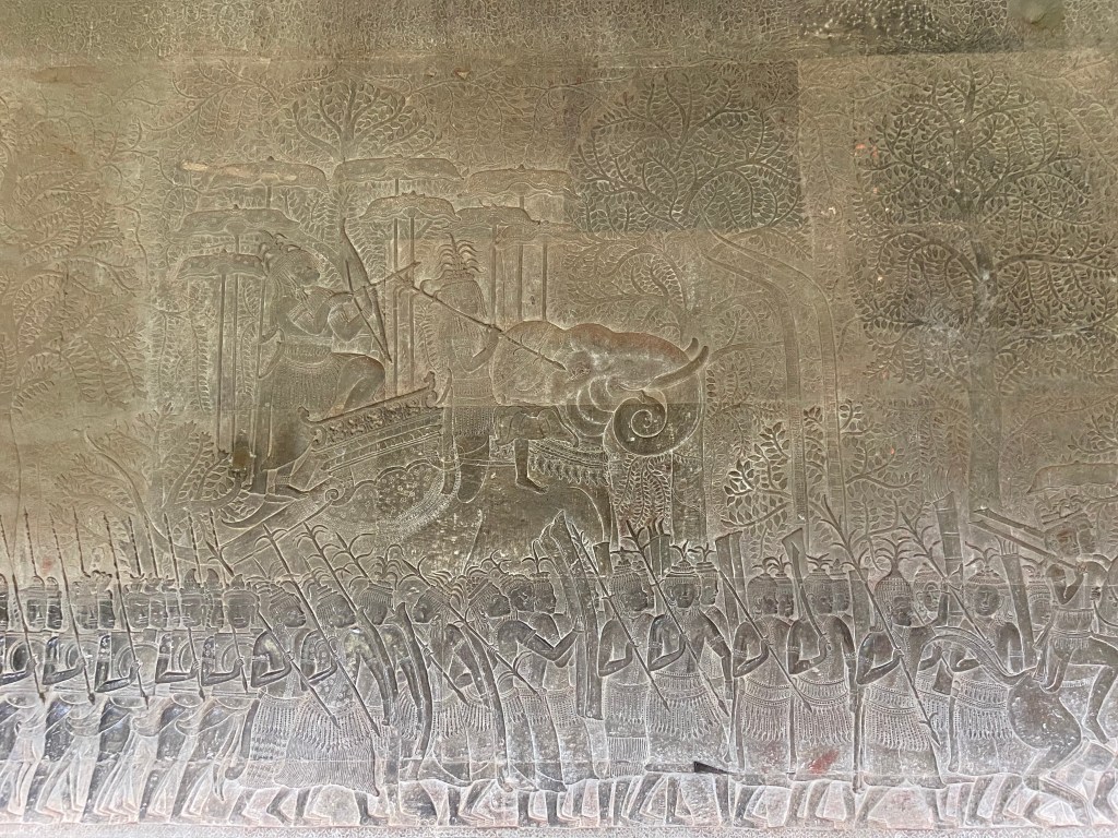 Ornate carving on stone inside the Angkor temple depicting a scene of men with spears and elephants. 