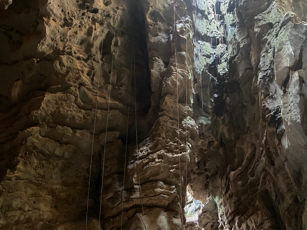 Top ropes up on some routes inside the Climbodia cave. There's a hole in the top with daylight streaming through as well as a exit to the outside of the crag. The rock is heavily featured limestone with horizontal breaks and large pockets. 