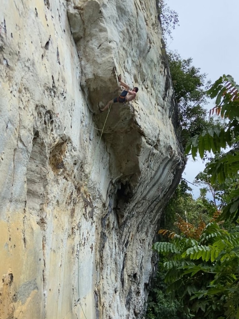 Climber using a heel hook to power through the short but steep roof section of a route at Cantabaco. The limestone is pretty featureless and is compact and bright white. 