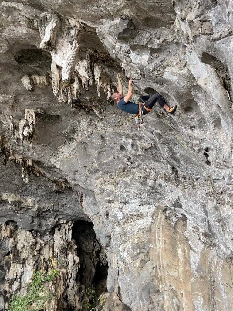 Climber flighting gravity through the steep white limestone of Buddha Cave. The cave is dripping with large tufas. 