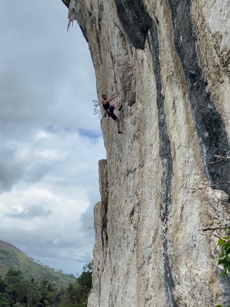 Climber using a high step on the white limestone wall at Igbaras. Below is a jungle filled valley. 