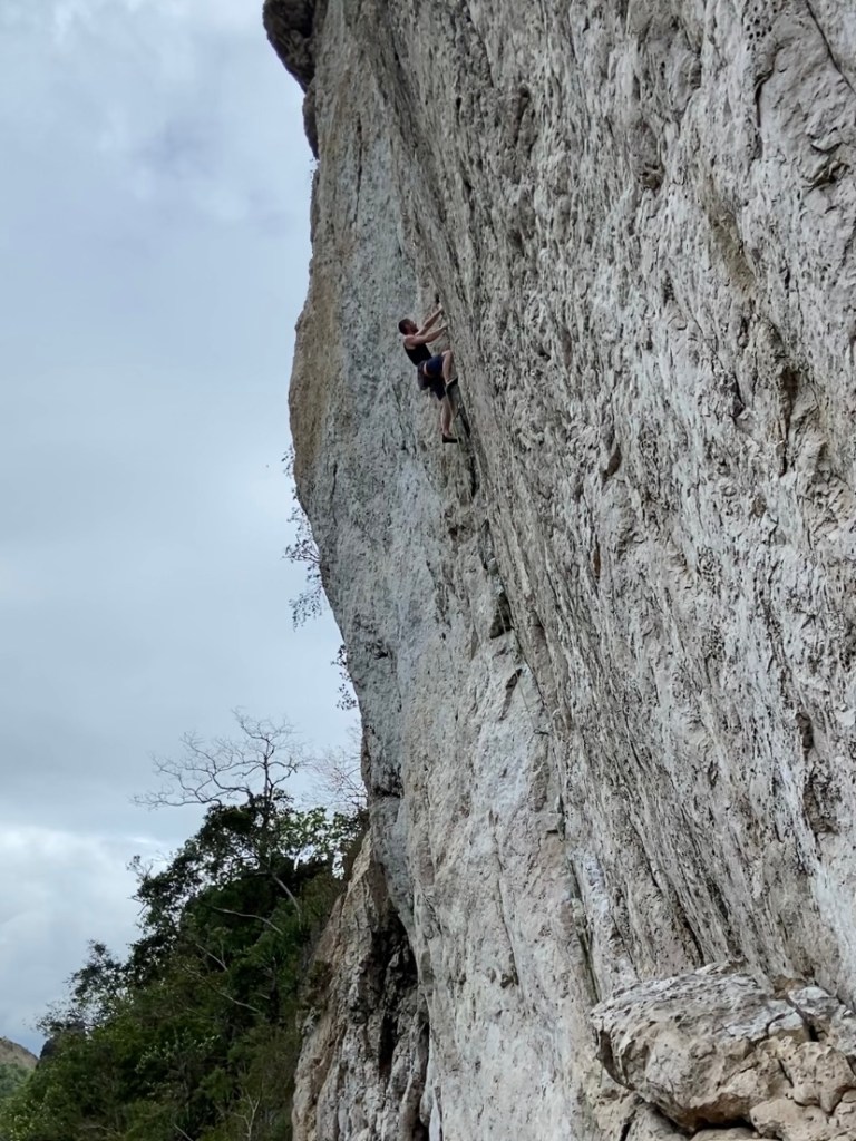 Climber working up the slanting crack feature on a grey limestone wall. 